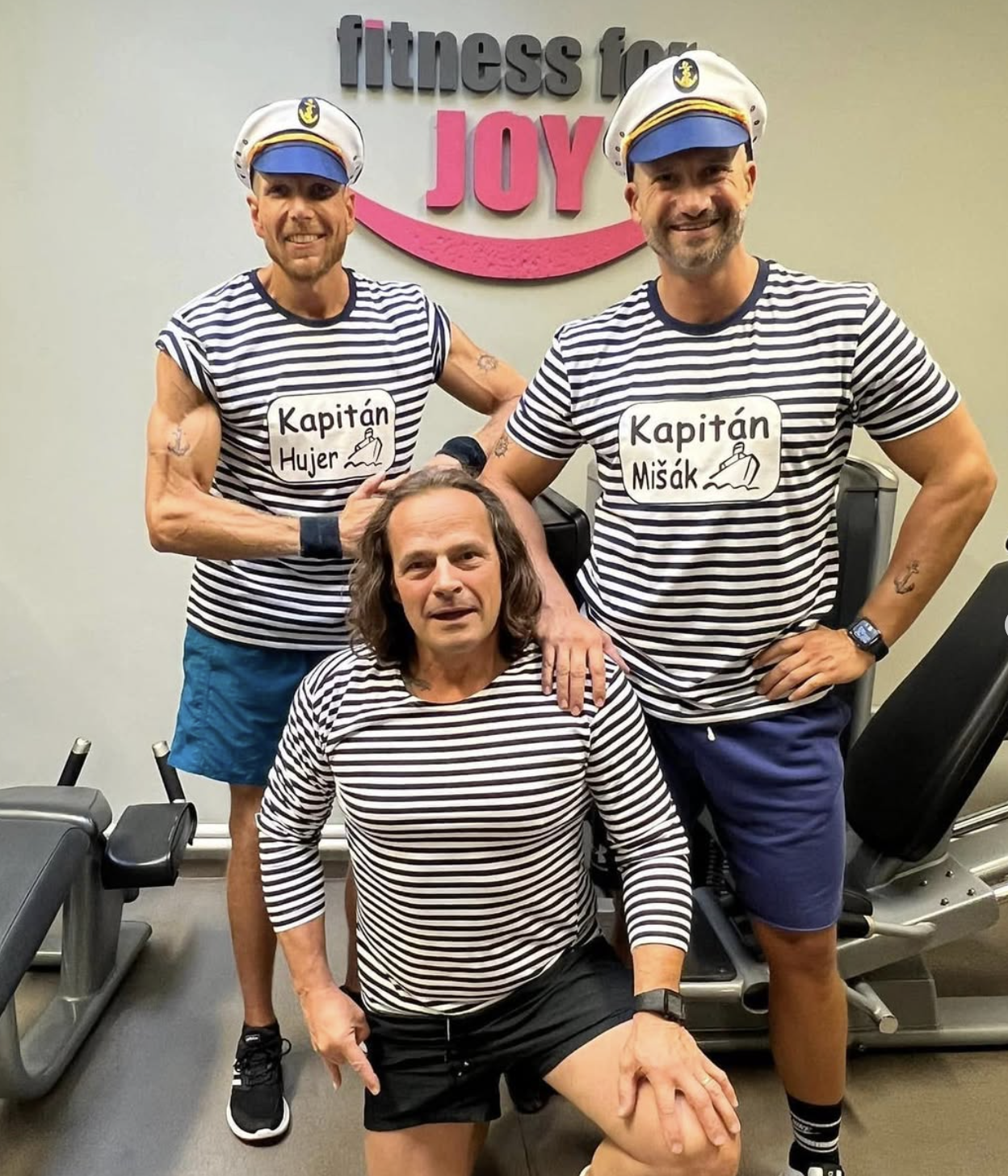 Tři muži v námořnických kostýmech s kapitánskými čepicemi